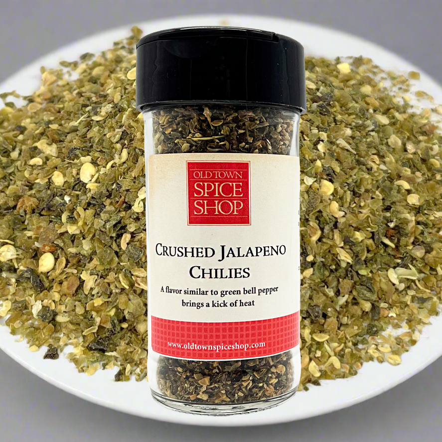 Jar of Old Town Spice Shop crushed jalapeno chilies on a plate with green herbs.