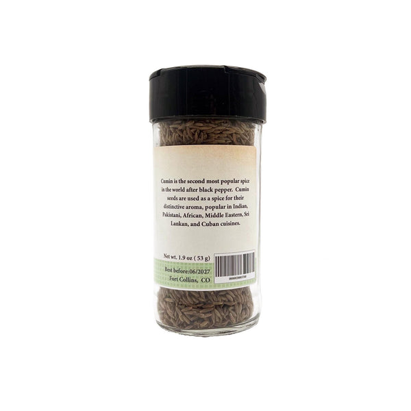 Glass jar of cumin seeds with a black lid on a white background