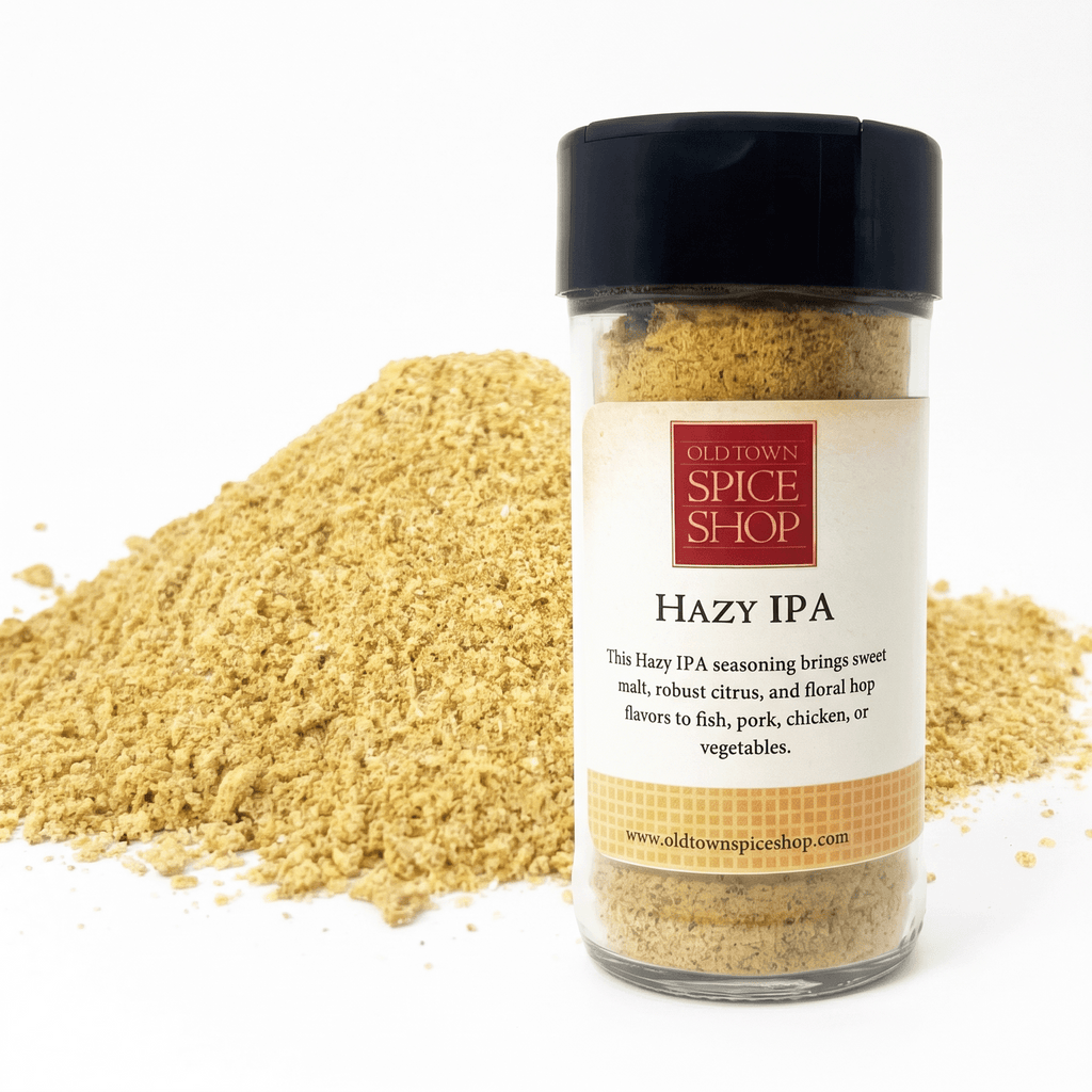 A clear plastic spice jar with a black lid labeled 'Old Town Spice Shop Hazy IPA' stands in front of a mound of the same light tan seasoning powder on a white background.