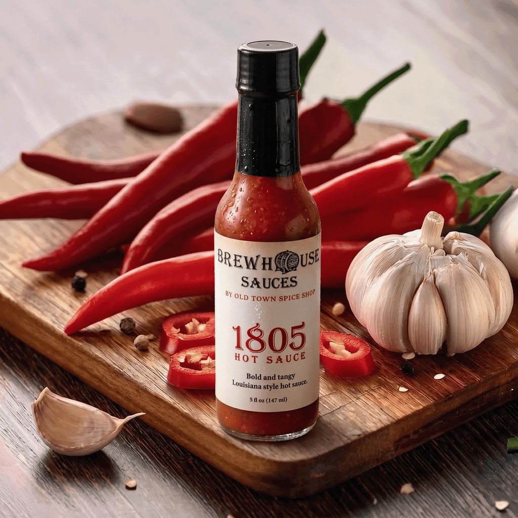 Bottle of Brewhouse Sauces 1805 Hot Sauce on a wooden cutting board with red peppers and garlic.