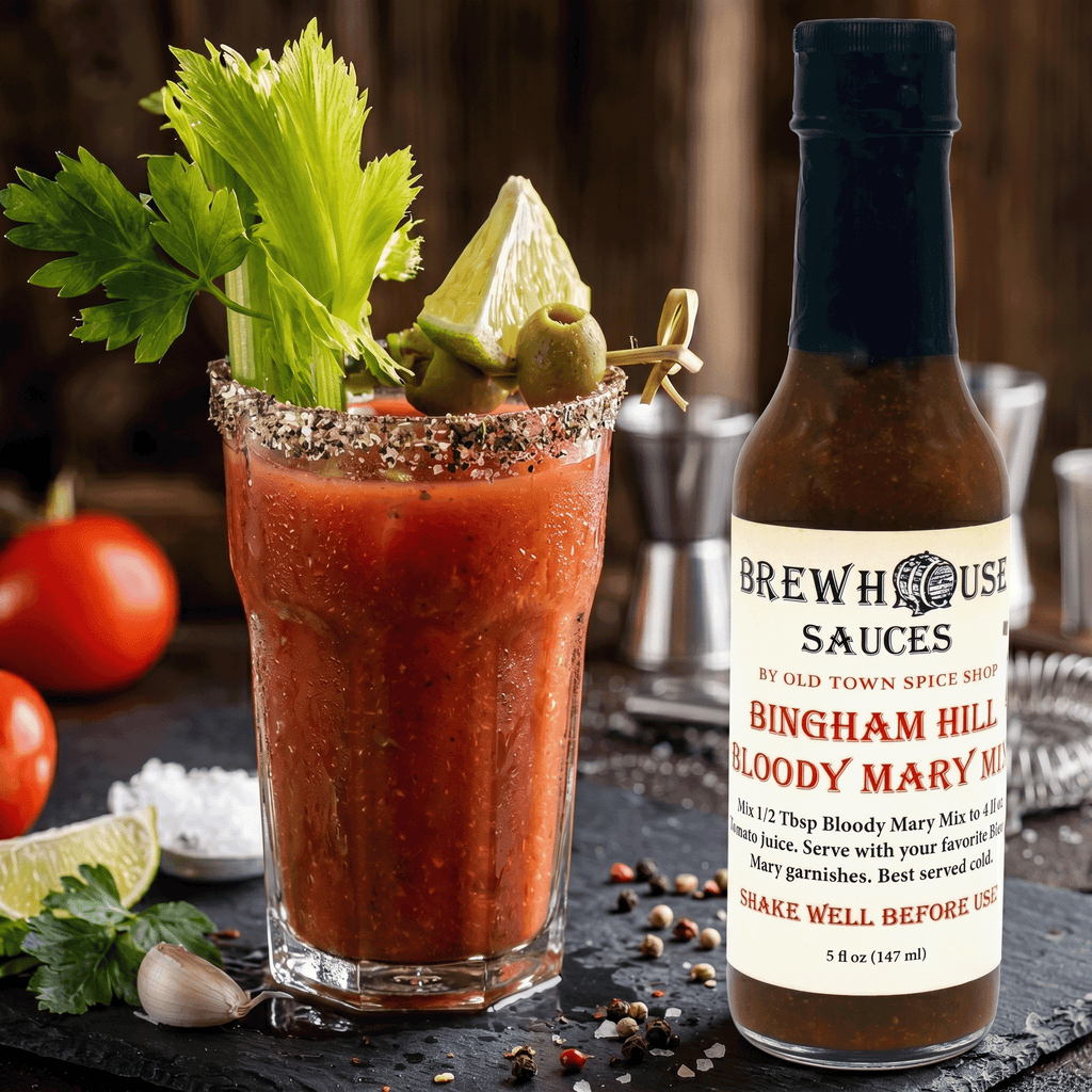 Bloody Mary cocktail with garnishes and a bottle of Bingham Hill Bloody Mary mix on a dark surface.