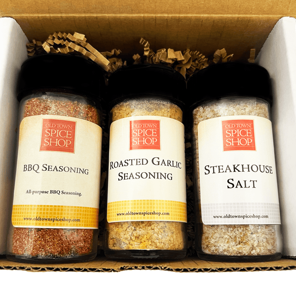 Three spice seasoning containers from Old Town Spice Shop arranged in a gift box with shredded paper filler. The containers include BBQ Seasoning, Roasted Garlic Seasoning, and Steakhouse Salt.