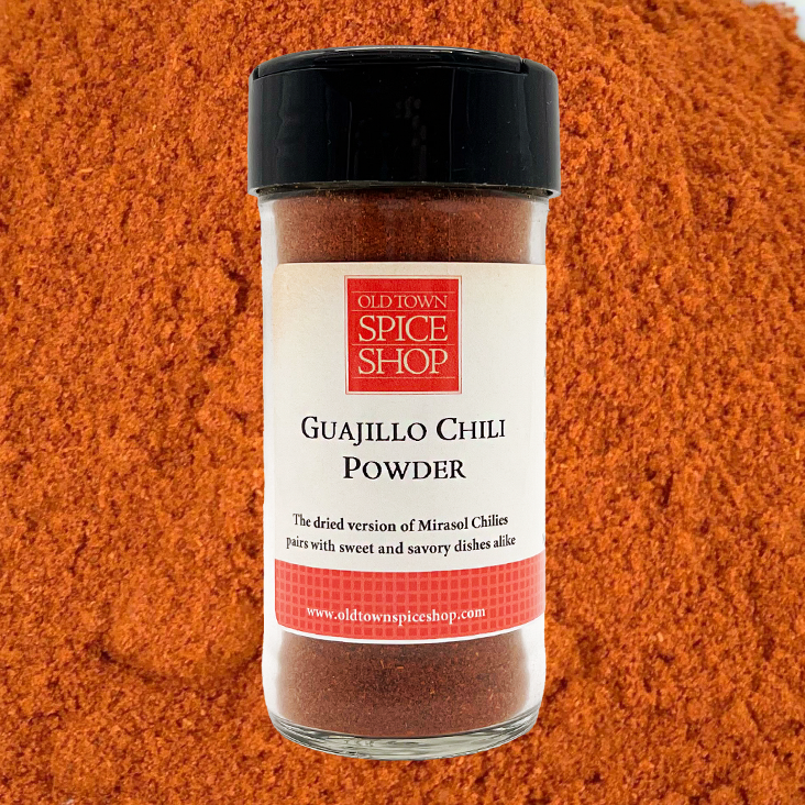 Bottle of Guajillo Chili Powder from Old Town Spice Shop on a background of red chili powder.