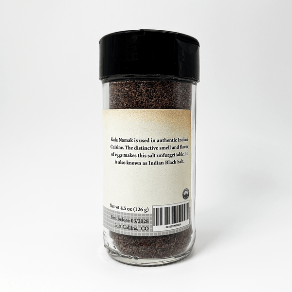 Glass jar of black salt with a label on a white background