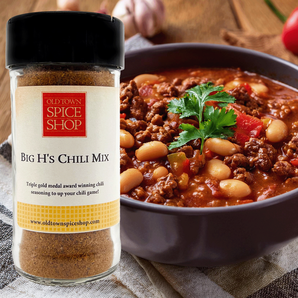 A bottle of 'Big H's Chili Mix' displayed next to a bowl of chili con carne garnished with parsley, tomatoes, and a spoon on the side.