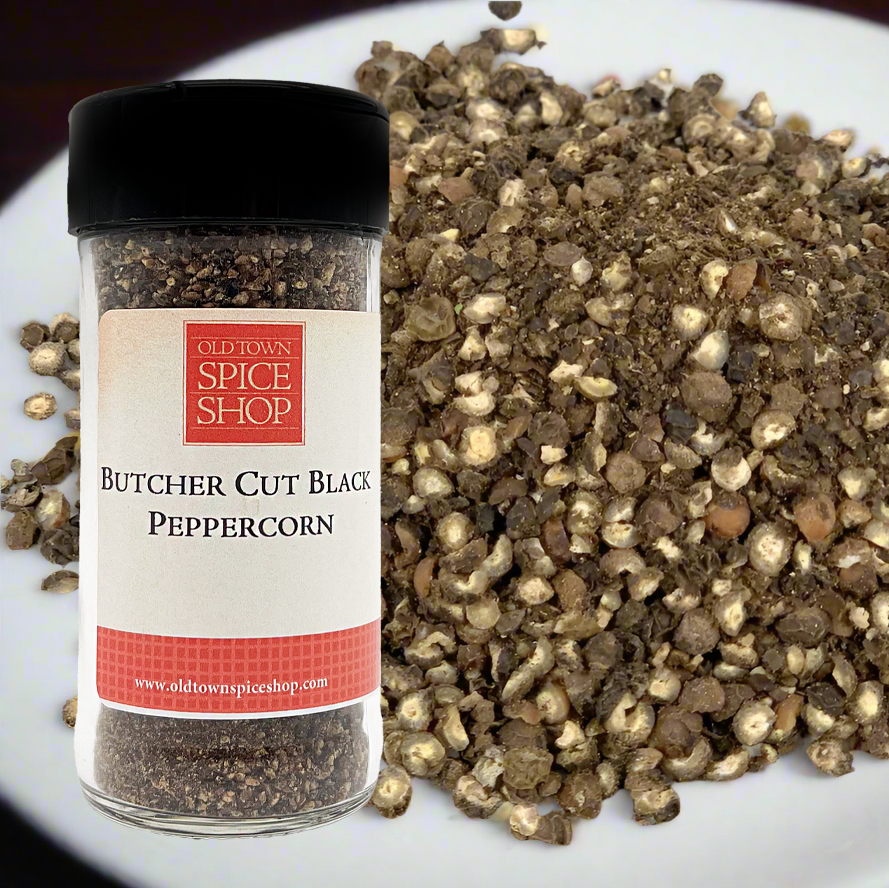 Butcher Cut Black Peppercorn container from Old Town Spice Shop on a white plate with peppercorns.