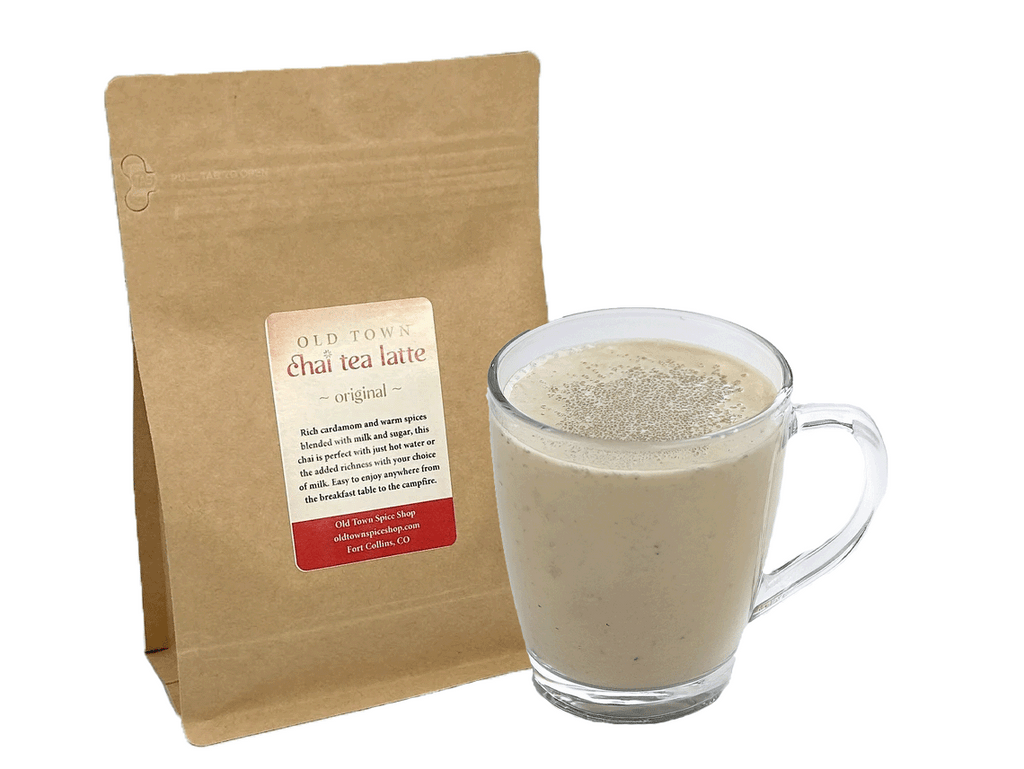 Glass mug of chai tea latte next to a brown paper bag with a label on a white background